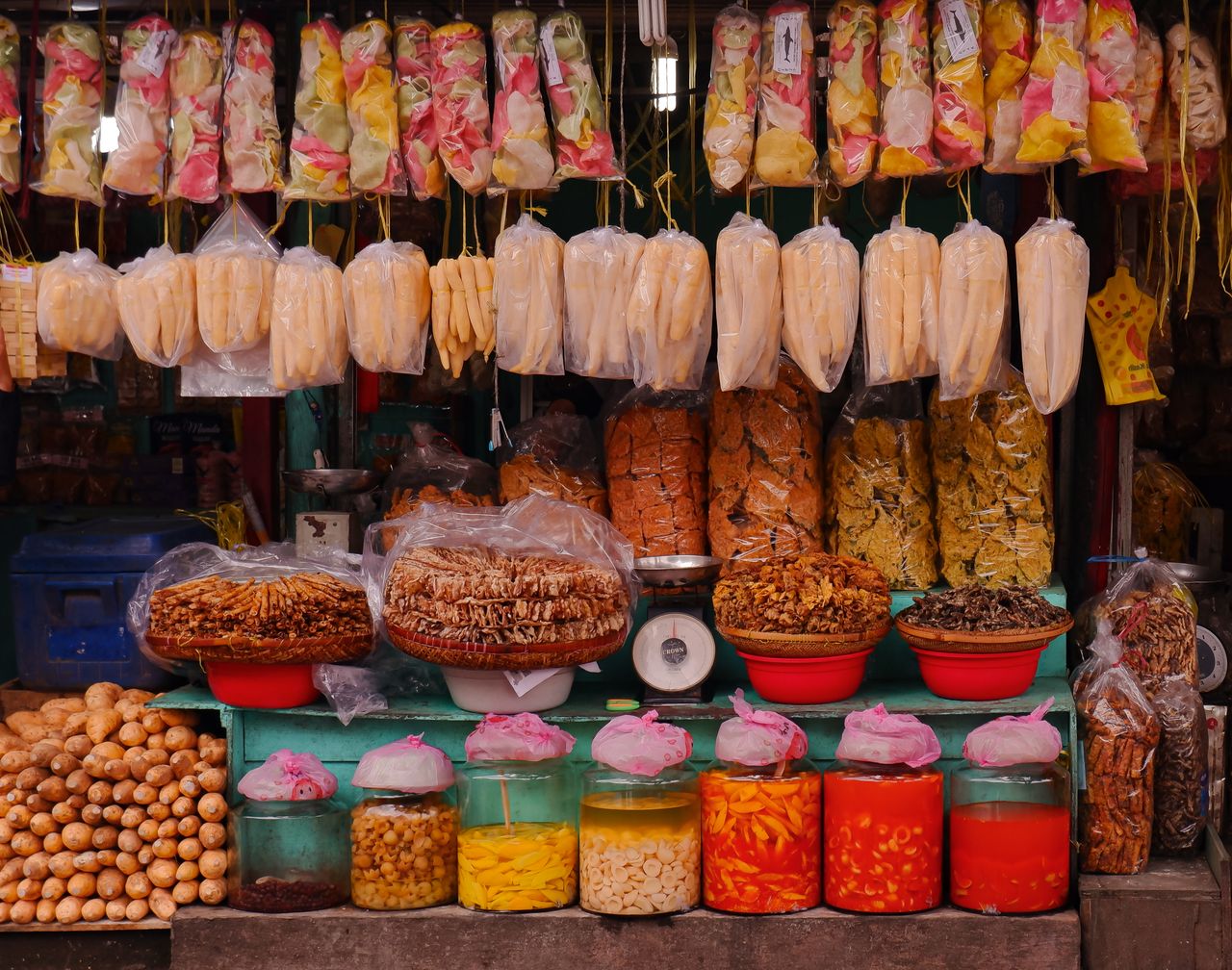 Vibrant display of snacks and produce at an Indonesian market stall, showcasing colorful and diverse goods.