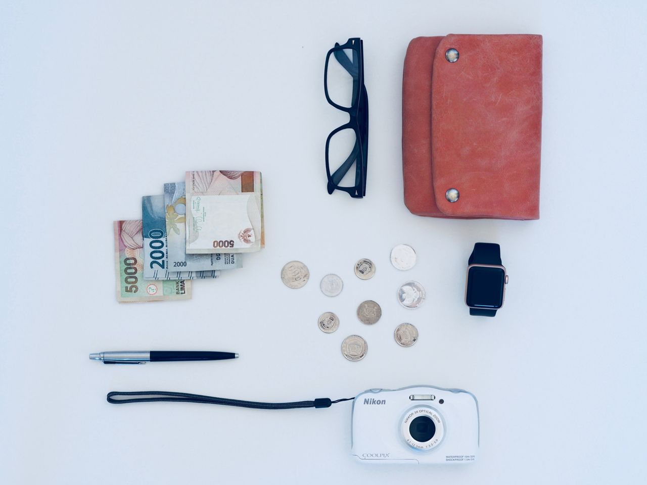 Flat lay of everyday items including currency, coins, wallet, and gadgets, all on a white background.